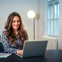 Cheerful woman using laptop at workplace.