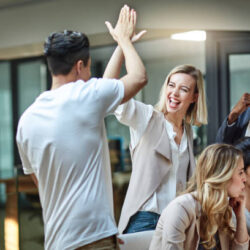 Shot of a group of colleagues giving each other a high five while using a computer together at work